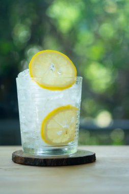 Bir bardak buz ve bir dilim taze limon, ahşap masa üzerinde, doğa arka planında. Soğuk yaz içeceği