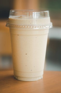 Sütlü kahve smoothie 'yi ahşap masada plastik bardakta kapat.