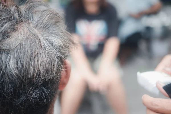 Back view of old man during haircut with people blur background