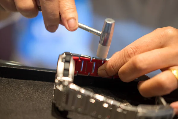 A watch pin being installed into the watch band with a hammer and a watch band holder. Close up