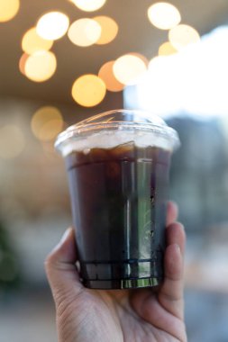 Bir el yaklaş ve bir bardak soğuk sade kahveyi kafenin arka planında tut. Bir kahve dükkanının reklamını yapma fikri