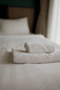 Bir otel odasında el değmemiş beyaz bir yatakta katlanmış beyaz havlular.