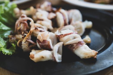 Tayland usulü ızgara kalamar, siyah tabakta sebzeli servis edilir.