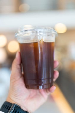 Elinde plastik bir fincan buzlu sade kahve.