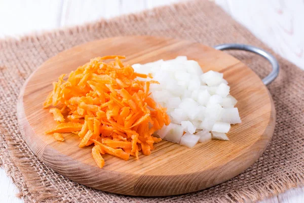 Onions and carrots chopped on a cutting board on a wooden table
