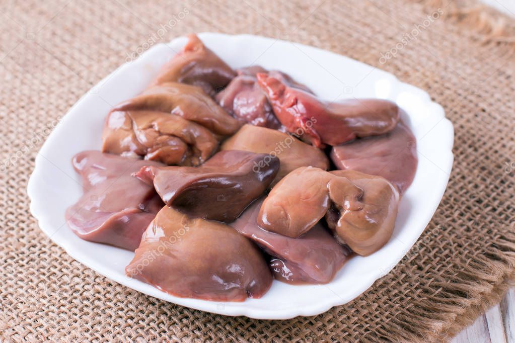 Fresh raw chicken liver on a plate. Wooden background.