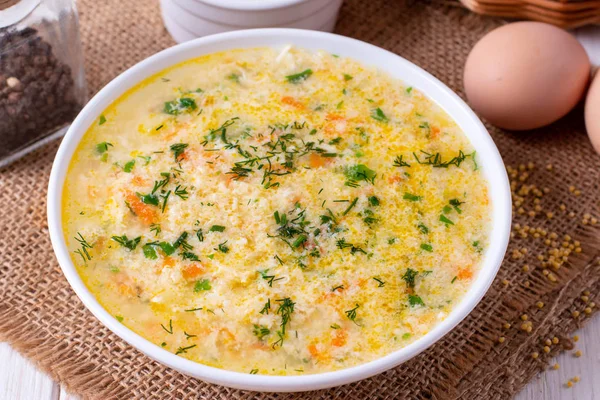 Soup kulesh with millet, potatoes and carrots in a white bowl on a napkin, parsley, dill on a wooden board background — Stock Image Soup Kulesh Millet Potatoes Carrots White Bowl Napkin Parsley Dill Royalty Free Stock Images