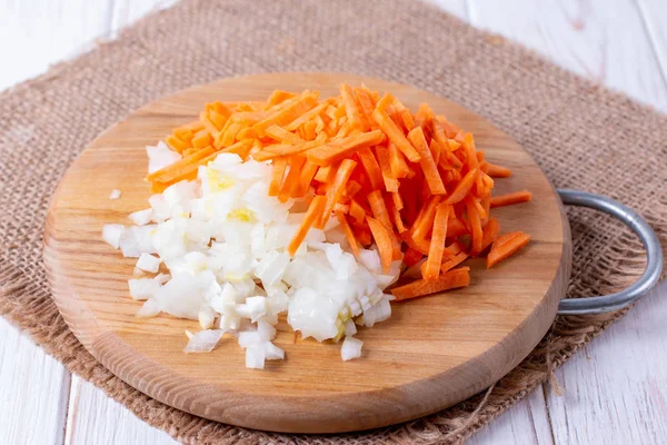Onions and carrots chopped on a cutting board on a wooden table — Stock Photo, Image