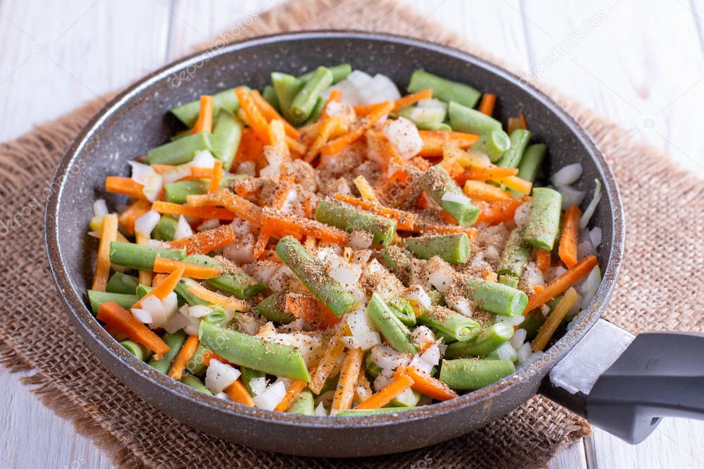 Onions, carrots, green beans and spices in a pan