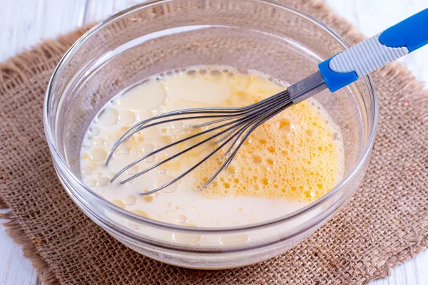 Ägg i en skål med visp och ost på ett träbord. — Stockfoto