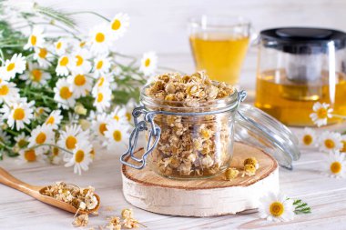 Beyaz ahşap masadaki kavanozda kurumuş papatya çayı. Organik papatya çayı ve çiçek.