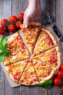 İnsanlar pizzadan bir dilim alıyor. Domatesli İtalyan pizzası, mozarella peyniri, ahşap bir masada mısır.