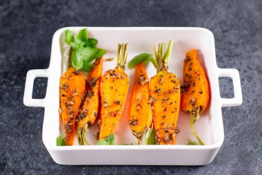 Karamelize edilmiş havuç ve fesleğen ile beyaz seramik formda koyu beton arka planda.