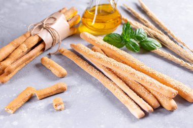 Grissini ekmekleri, fesleğen yaprakları ve zeytinyağıyla iştah açıcı bir şekilde masaya uzanıyor. Lezzetli ve sağlıklı organik yiyecekler..