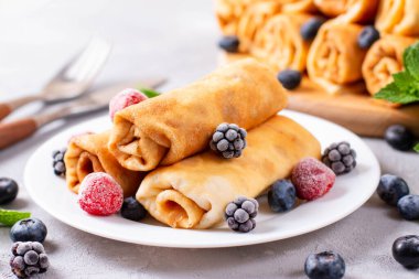 Beyaz tabakta süzme peynir ve böğürtlen dolu krepler. Sarılmış gözleme.