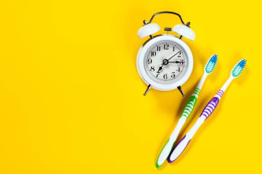 Diş temizliği konsepti. İki diş fırçası ve sarı arka planlı çalar saat..