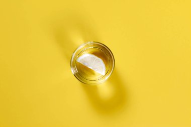 Sarı arka planda limonlu bir bardak su. Düz konum, üst görünüm, kopyalama alanı