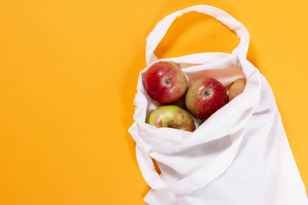 Organic apples in cotton bag on a color background. Flat lay, top view, trendy background.