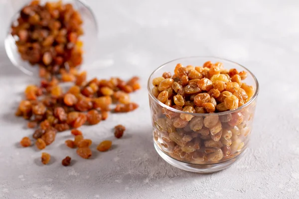Dried and wet raisins in a glass beaker on a light background