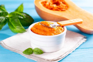 Kaşık ile seramik kasede kabak püresi, mavi tahta üzerinde sağlıklı bir tatlı.