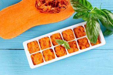 Düz kompozisyonda, buz kalıplarında püre bebek mamasıyla mavi ahşap masada yatıyordu. Üst görünüm.