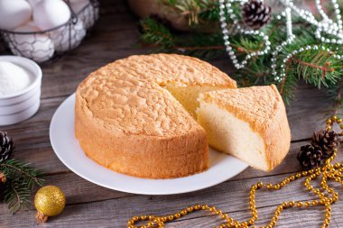 Yeni yıl ve Noel pastası ya da şifonlu kek beyaz tabakta çok yumuşak ve lezzetli malzemelerle: yumurta, un, ahşap masa sütü. Arkaplan ve duvar kağıdı için ev yapımı fırın kavramı.