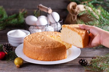 Noel ağacı dalları, koniler ve oyuncaklarla ahşap bir masada beyaz bir tabakta ev yapımı pandispanya. Yeni yıl ve Noel tatlısı. Pasta..