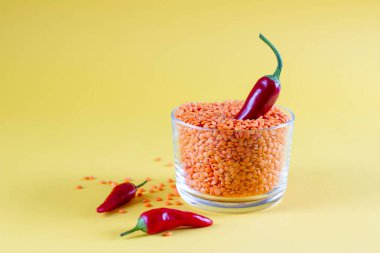 Sarı arka planda kırmızı biberli cam bir kavanozda kırmızı mercimek. Sağlıklı gıda konsepti, renk eğilimi, gıda duvar kağıdı