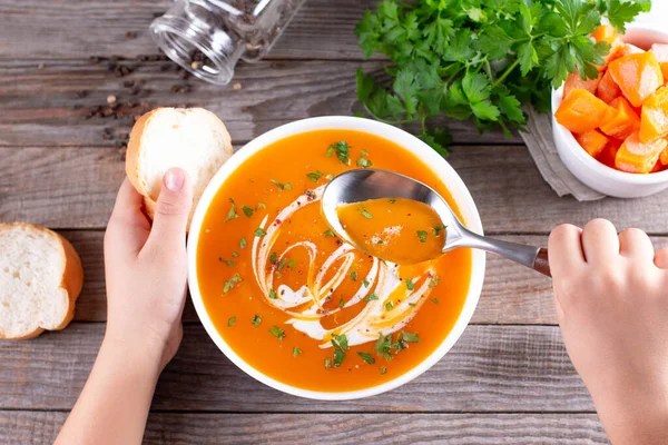 A hand holding a spoon of pumpkin soup with a white soup bowl. Croutons and pumpkin in the background. Autumn Winter food — Stock Image Hand Holding Spoon Pumpkin Soup White Soup Bowl Croutons Pumpkin Stock Photo