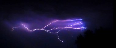 Karanlık gökyüzünü aydınlatan dallanmış yıldırımlar.