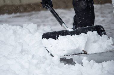 Birisi kışın kar yağarken dışarıda kar kürüyor.