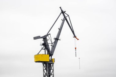 Beyaz gökyüzünün önündeki limanda bir vinç çalışıyor.