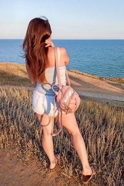 Genç esmer kadın arkasını dönüp denize bakıyor..