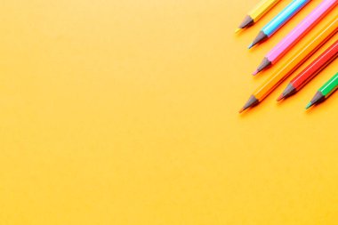 Turuncu arka planda çok renkli kalemler. Güzel sanatlar derslerinde renkli kalemlerle çizimler. Okul için hazırlık.