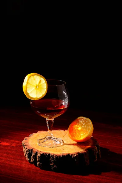Ahşap arka planda limonlu bir bardak konyak. Kesme tahtasında dilimlenmiş limon ve bıçak..