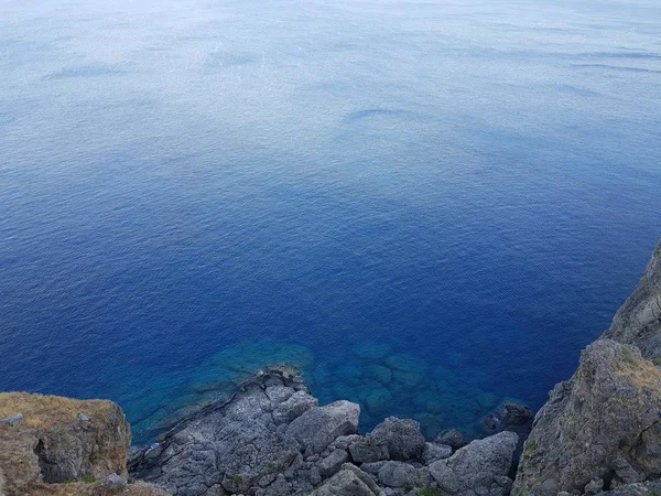 De arriba tiro de agua azul limpia de mar tranquilo cerca del acantilado pedregoso áspero en día soleado en la naturaleza hermosa . —  Fotos de Stock