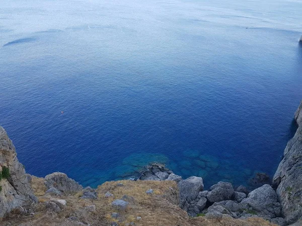 De arriba tiro de agua azul limpia de mar tranquilo cerca del acantilado pedregoso áspero en día soleado en la naturaleza hermosa . —  Fotos de Stock