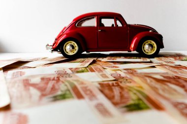 Rus para banknotlarının arka planında kırmızı oyuncak araba. Veresiye ve taksitle yeni bir araba almak. Üzerinde 5000 ruble yazan Rus banknotları. Kapatın. İş, finans kavramı. İzole edilmiş