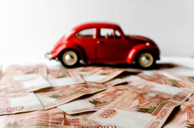 Rus para banknotlarının arka planında kırmızı oyuncak araba. Veresiye ve taksitle yeni bir araba almak. Üzerinde 5000 ruble yazan Rus banknotları. Kapatın. İş, finans kavramı. İzole edilmiş
