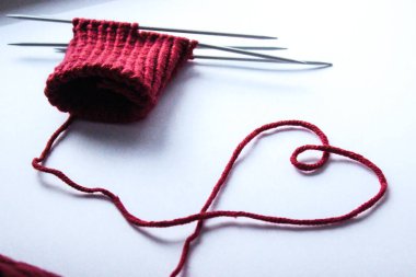 Tamamlanmamış yün ve örgü iğnesi tasarımı. Kırmızı iplik ve arapsaçı. El yapımı konsept. El işi afişi. Aşk, romantik, sevgililer günü konsepti. Kalp şeklindeki iplik izole edilmiş. Üst Manzara. Boşluğu kopyala
