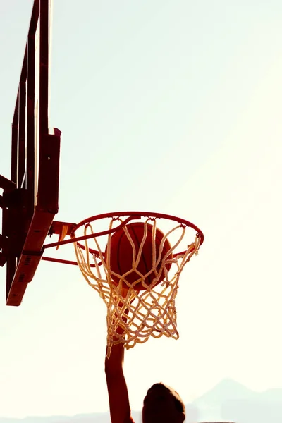 잘 알려 지지 않은 실루엣을 한 농구 선수는 해 가질 때 골대에 도달 한다. 목표 성취 개념. — 스톡 사진