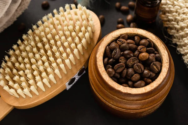 Coffee peeling. Home spa concept. Coffee beans and body brush for anti-cellulite massage for skin treatment on black background. Home spa concept