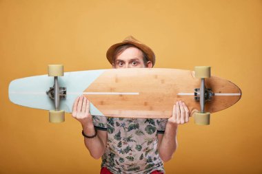 Hasır şapka ve bir longboard arkasında yarım yüzle tropikal t-shirt giymiş kahverengi gözlü genç adam portresi stüdyo