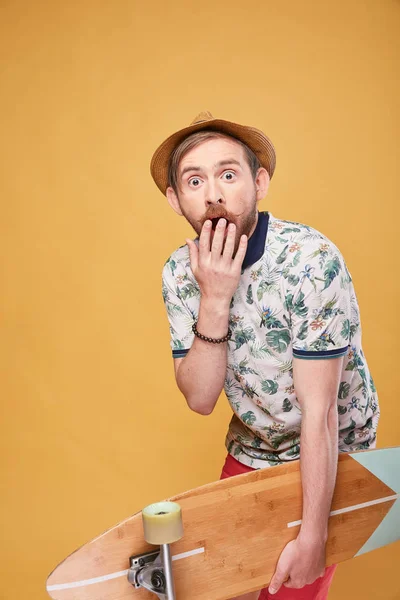 苺髭手に熱帯のプリント ポロシャツ 赤いショート パンツとロングボードでの麦わら帽子に身を包んだ若い男 黄色の背景で撮影スタジオ — ストック写真
