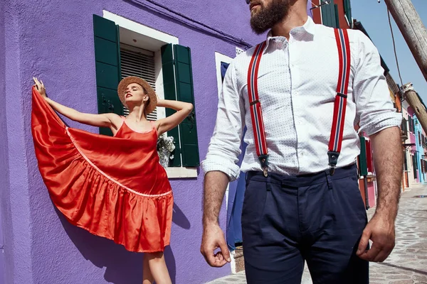 一对夫妇附近的紫罗兰房子在布拉诺岛 威尼斯 意大利 红色浪漫礼服的妇女 稻草哈 人在白色圆点衬衣 和长裤与红色吊带 — 图库照片