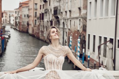 Venedik kanal üzerinde bir köprü üzerinde poz güzel gülümseyen gelin zarif, lüks Fildişi elbise ve kabarık saç modeli içinde