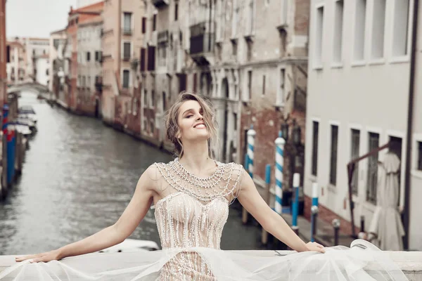 美丽的微笑新娘优雅 豪华象牙礼服和发髻的发型 摆在一座桥上的运河在威尼斯 — 图库照片