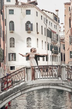 Venedik kanal üzerinde bir köprü üzerinde poz güzel düğün çifti. Zarif, lüks Fildişi elbise ve kabarık saç modeli, nişanlısı geen takım içinde gelin