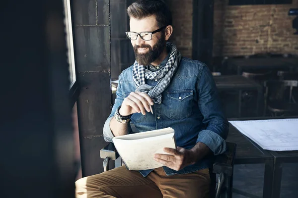 Smiling male writer journalist with dark hair and beard in denim jacket is sitting in public place and creating new article