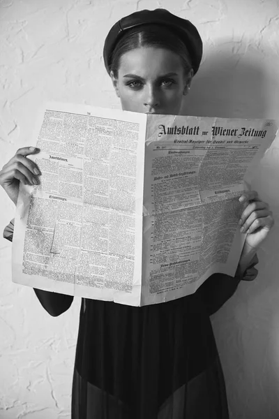Black and white portrait of beautiful woman in newsboy cap with vintage newspaper in hands. Retro style